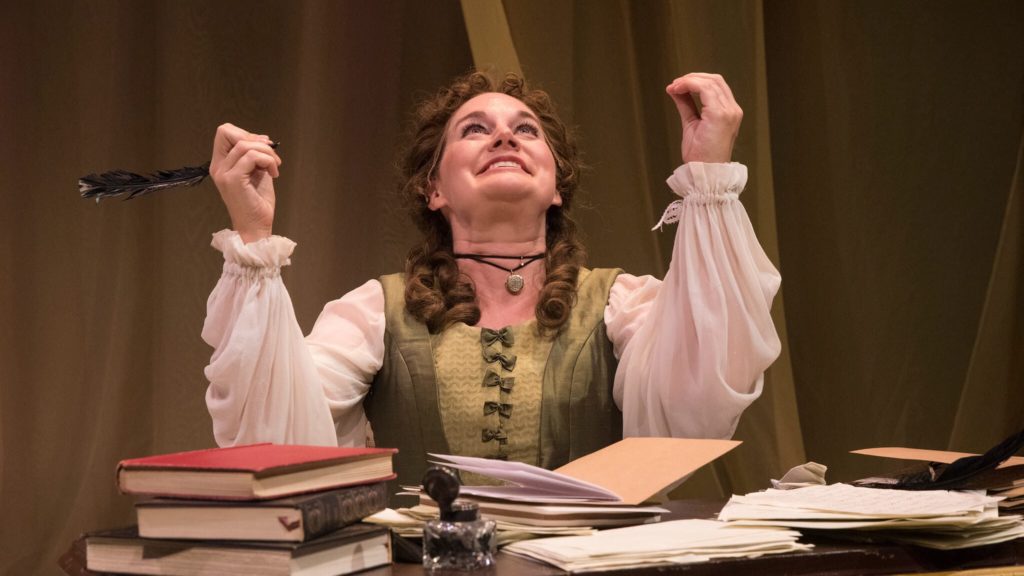 Woman in historical french clothes holds a quill and looks upwards for inspiration